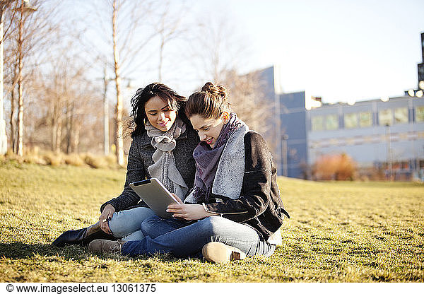 Female friends using digital tablet on grassy field