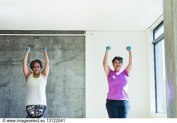 Female friends using dumbbells while exercising against wall in yoga studio