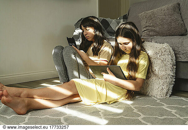 Female friends using gadgets in living room at home