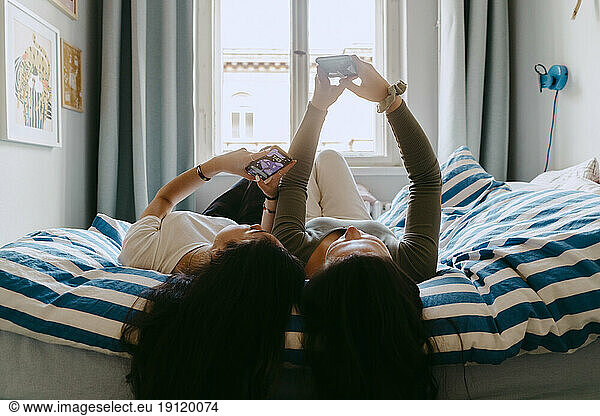 Female friends using smart phone while lying on bed at home