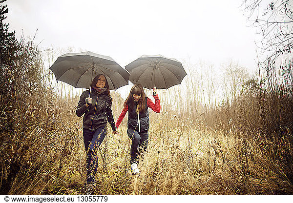 Female friends walking with umbrellas on grassy field against sky