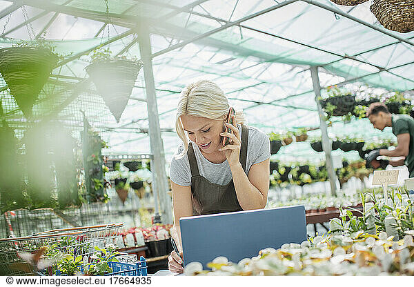 Female garden shop owner talking on smart phone at laptop