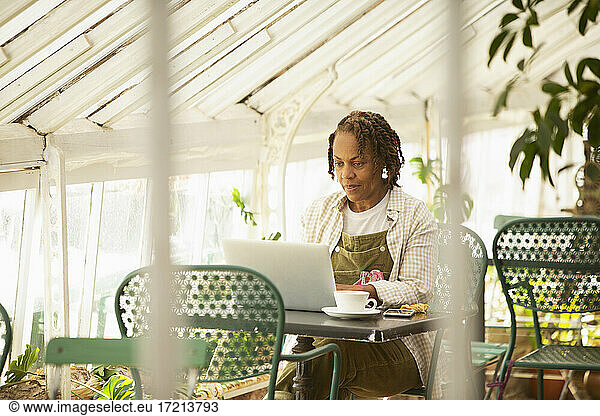 Female garden shop owner working at laptop in greenhouse