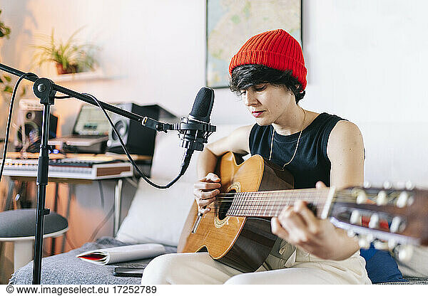 Female guitarist wearing knit hat while playing guitar at studio