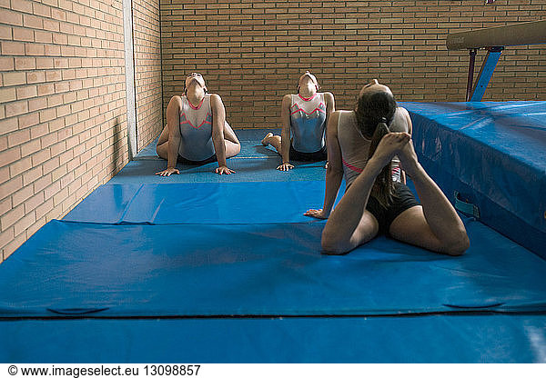 Female gymnasts bending over backwards while exercising in gym