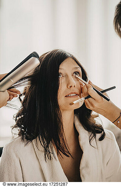 Female hairdresser and make-up artist preparing bride for wedding ceremony
