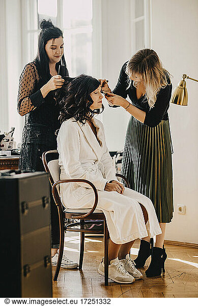 Female hairdresser and make-up artist with bride at studio