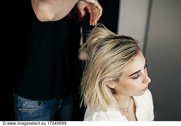 Female hairstylist doing hairstyle of blond model in studio
