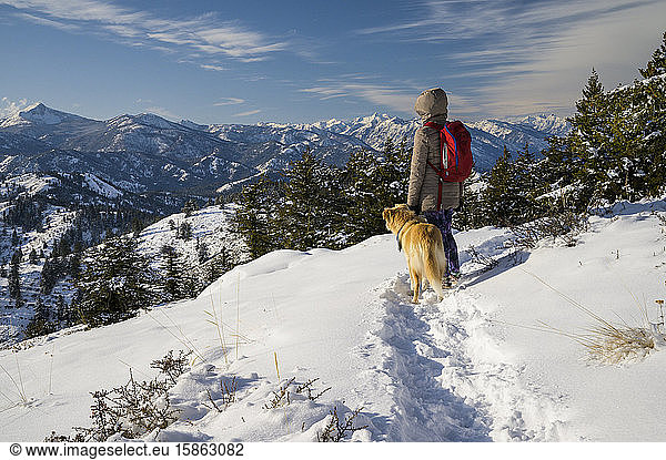 Female Hiker and Dog Looking Into Distance In Snowy Mountain Scene
