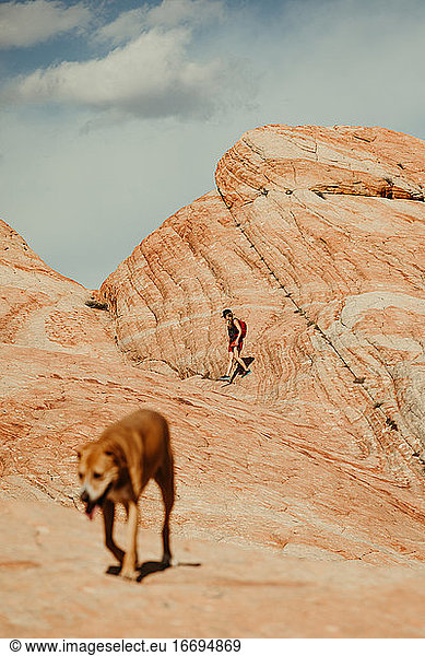 female hiker in focus with dog in foreground in red rocks desert