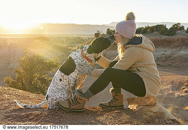 Female hiker kissing dog while in the desert during sunset