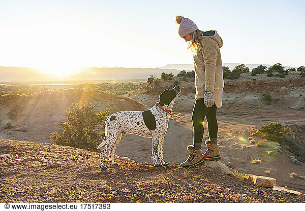 female hiker looking at dog while standing in desert during sunset