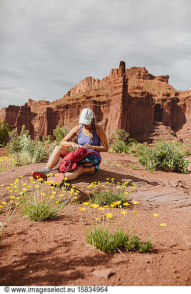 female hiker sits down in yellow flowers at fisher towers moab utah
