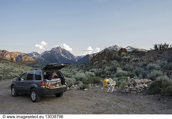 Female hiker sitting in sports utility vehicle against Mount Morrison