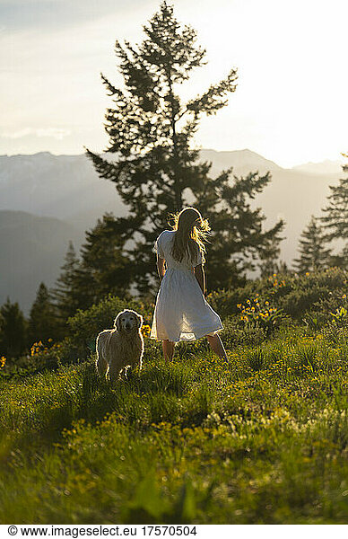 Female in a dress standing with her dog in the mountains