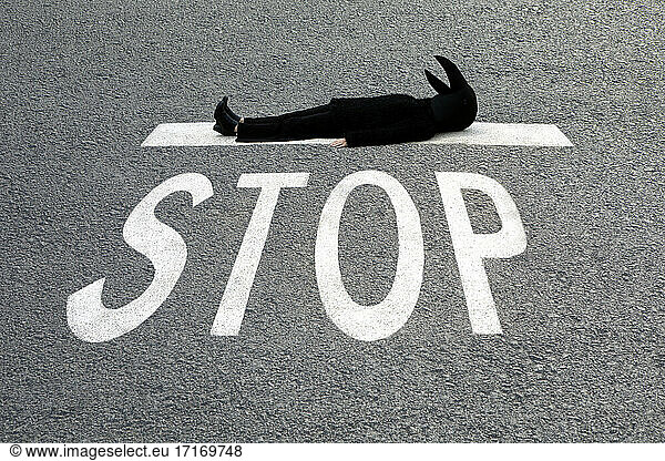 Female in crow costume lying down at STOP sign on road