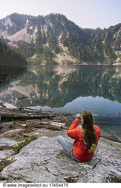 Female In Red Coat Drinking Coffee Next To An Alpine Lake