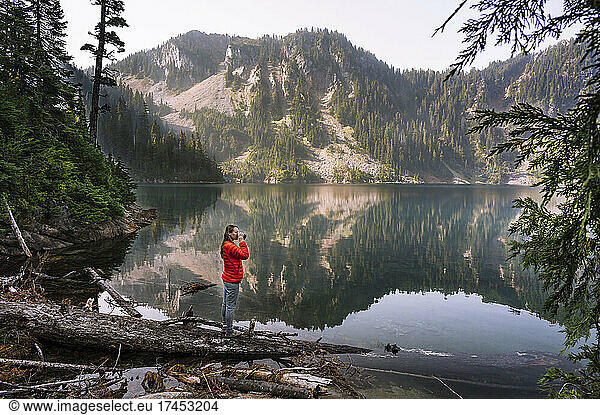 Female In Red Puffy Jacket Drinking Coffee Next To Alpine Lake