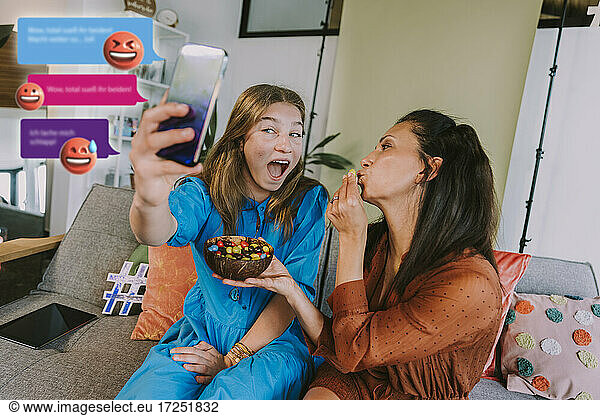 Female influencer filming with friend through mobile phone at home