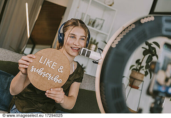 Female influencer showing like and subscribe sign while vlogging at home