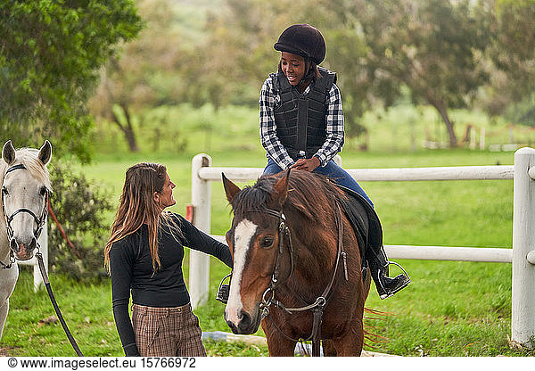 Female instructor teaching horseback riding to girl in rural paddock
