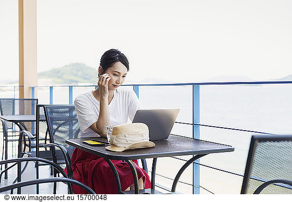 Female Japanese professional sitting on balcony of a co-working space  using laptop computer.