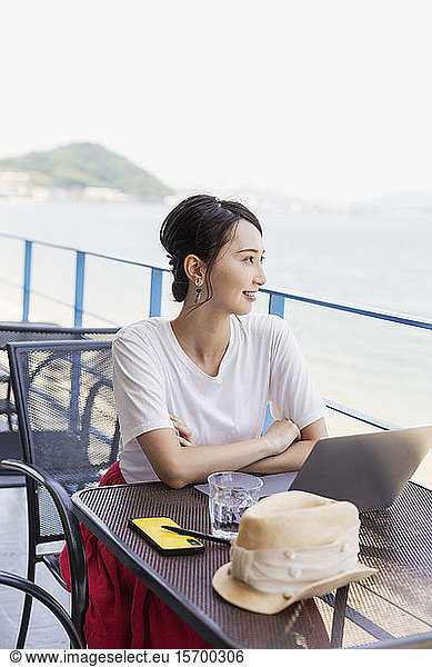 Female Japanese professional sitting on balcony of a co-working space  using laptop computer.