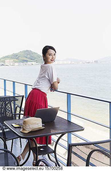 Female Japanese professional standing on balcony of a co-working space  laptop computer on table.