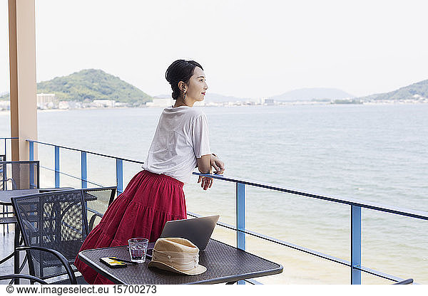 Female Japanese professional standing on balcony of a co-working space  laptop computer on table.