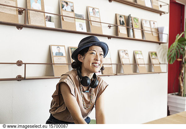 Female Japanese professional wearing Trilby hat and headphones sitting in a co-working space.