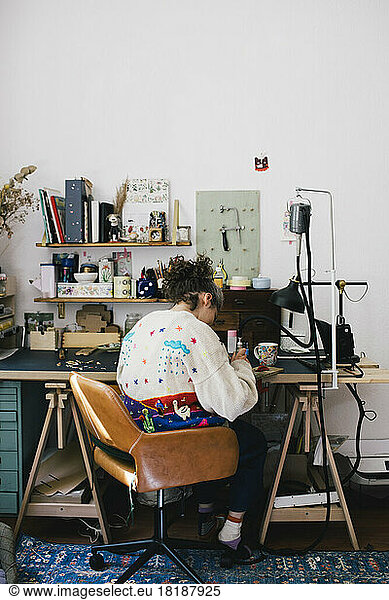 Female jewelry maker sitting on chair while working at home