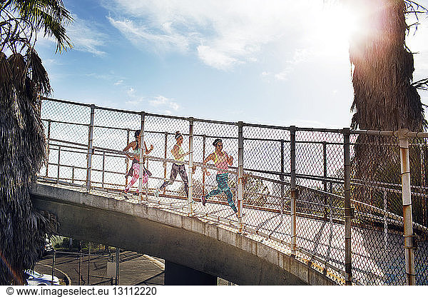 Female joggers on bridge against sky on sunny day