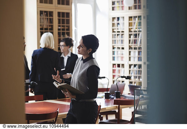 Female lawyer gesturing while coworkers standing in background at library