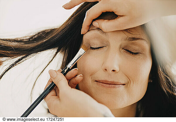Female make-up artist applying eye shadow on bride's eyes at studio
