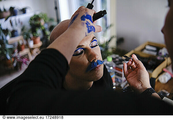Female make-up artist applying makeup on male model at studio