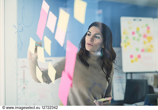 Female mature engineer writing on adhesive note stuck to glass in office