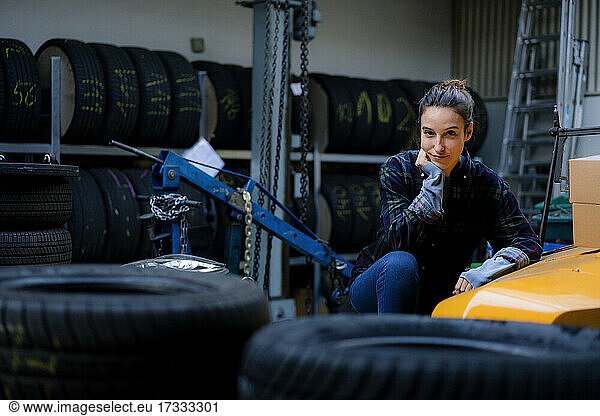 Female mechanic with hand on chin crouching by toy car at workshop