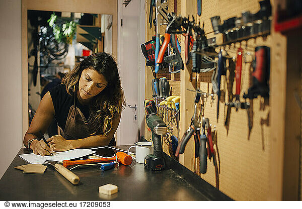 Female mechanic writing on paper at repair shop