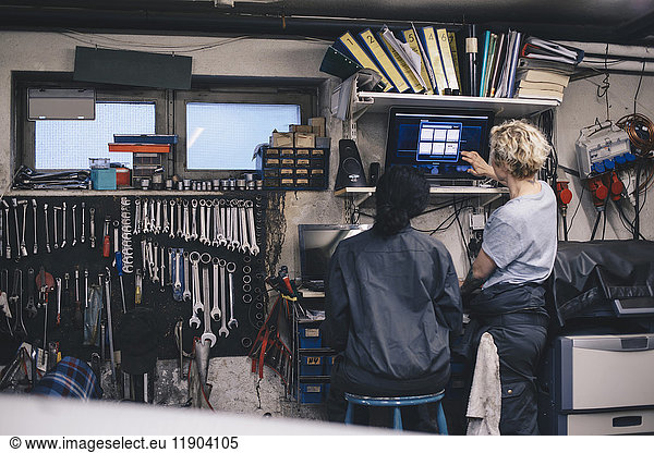 Female mechanics discussing over computer monitor at auto repair shop