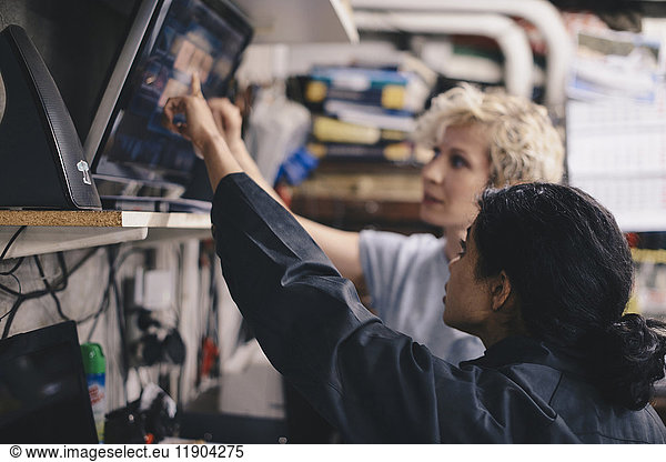 Female mechanics pointing at computer monitor while discussing in auto repair shop