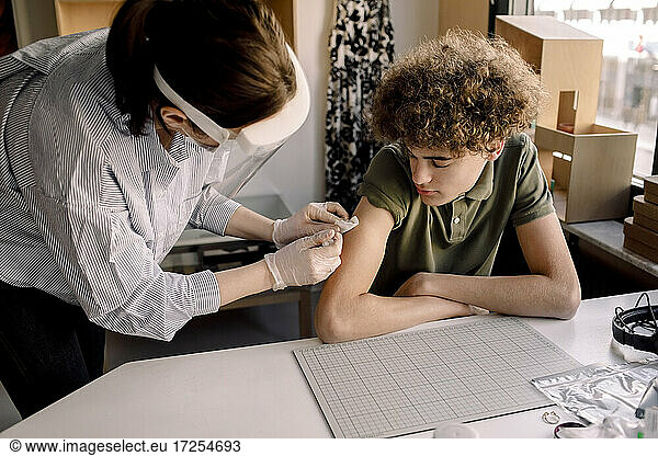 Female medical worker injecting COVID-19 vaccine to teenage boy at home