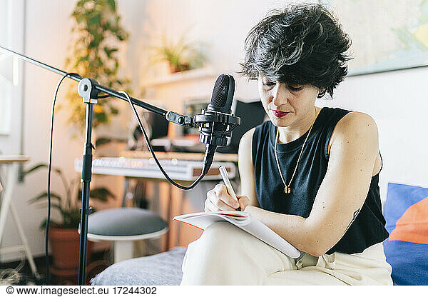 Female music composer writing in notepad while recording at studio