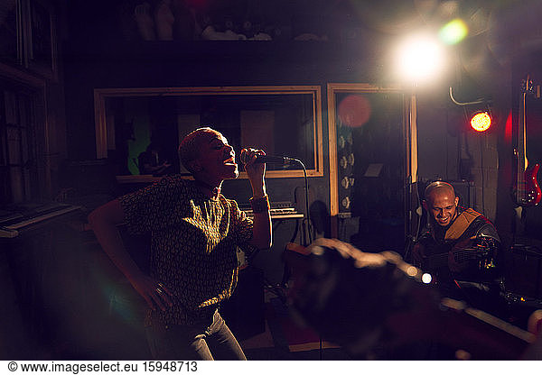 Female musician singing into microphone in dark recording studio