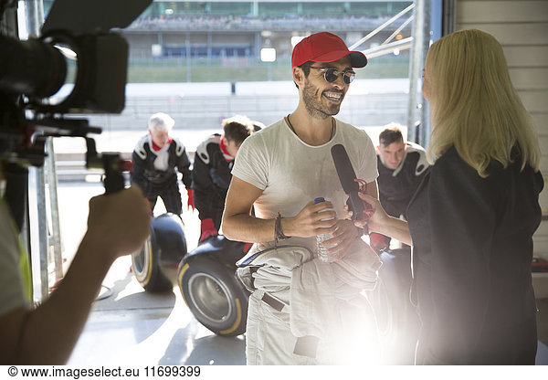 Female news reporter interviewing male formula one race car driver in repair garage
