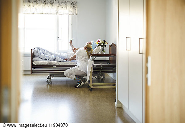 Female nurse and senior man taking selfie with smart phone in hospital ward