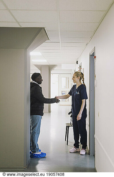 Female nurse doing handshake with male patient while standing in hospital corridor