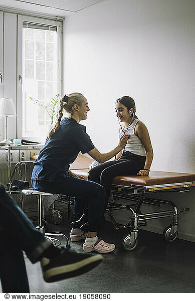 Female nurse examining girl sitting on bed in clinic