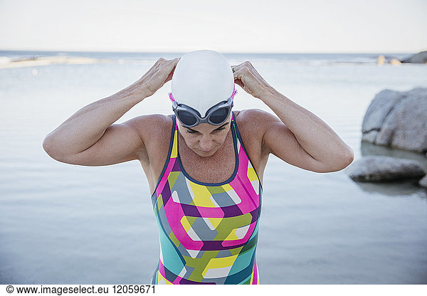 Female open water swimmer adjusting swimming goggles at ocean