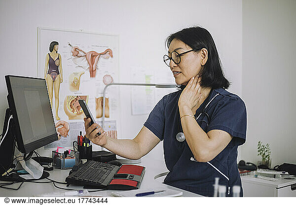 Female otolaryngologist on video call through smart phone doing online consultation while explaining throat in clinic