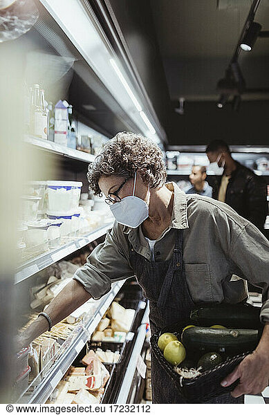 Female owner arranging food product on rack in delicatessen shop during pandemic